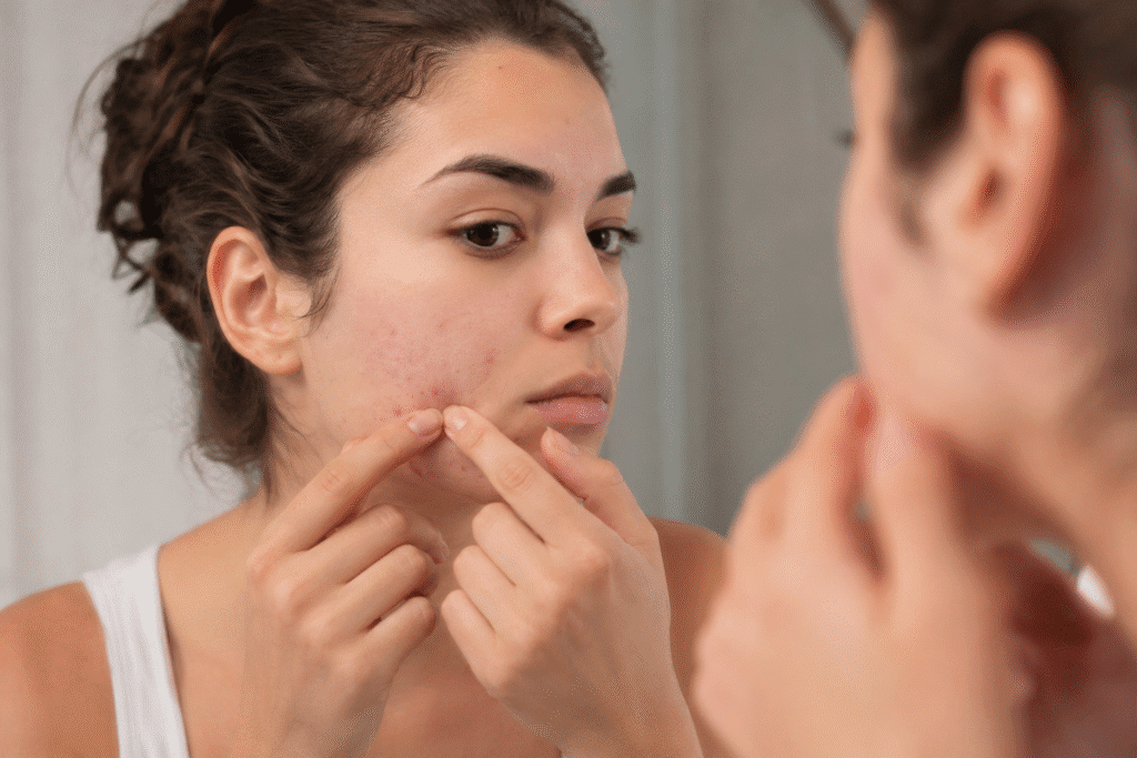 Woman picking a pimple on her cheek in front of a mirror.